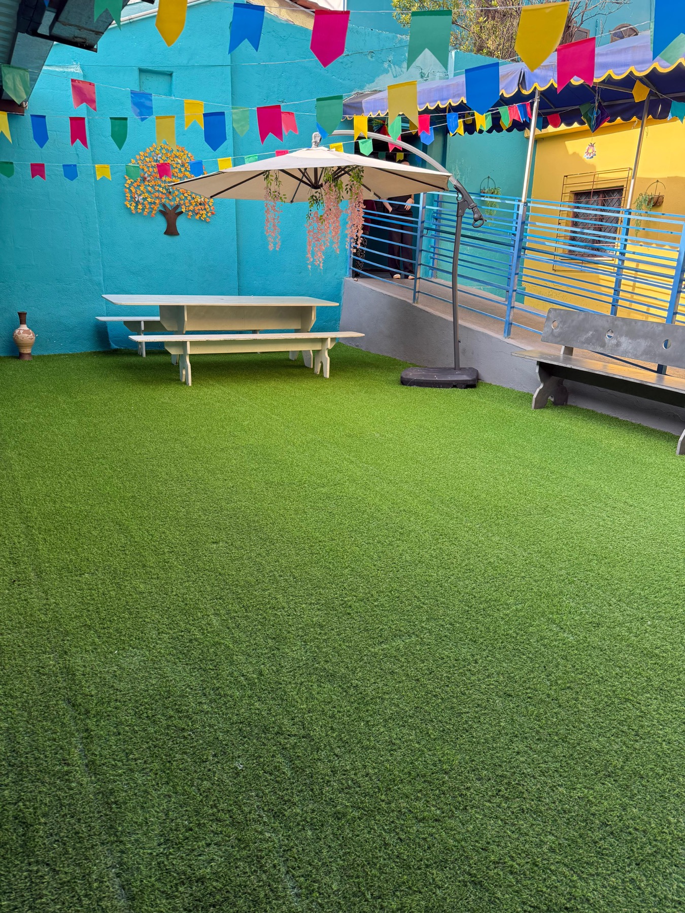 Área externa decorada com gramado, mesa e guarda-sol